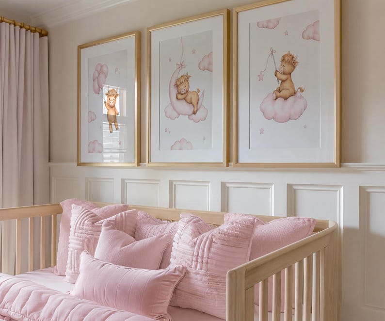 K&ouml;nnte beinhalten: Drei gerahmte Kunstdrucke mit goldenen Rahmen, die jeweils eine skurrile Illustration eines Baby-Tiers auf einer Wolke zeigen. Die Drucke befinden sich in einem Kinderzimmer, &uuml;ber einem hellen Holzbett mit rosa Bettw&auml;sche und Kissen.