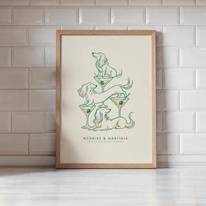 May include: A framed art print featuring three long-haired dachshunds interacting with martini glasses. The illustration uses green and gold lines on a cream background. The text reads WEENIES & MARTINIS and GOOD DRINKS, BETTER COMPANY.