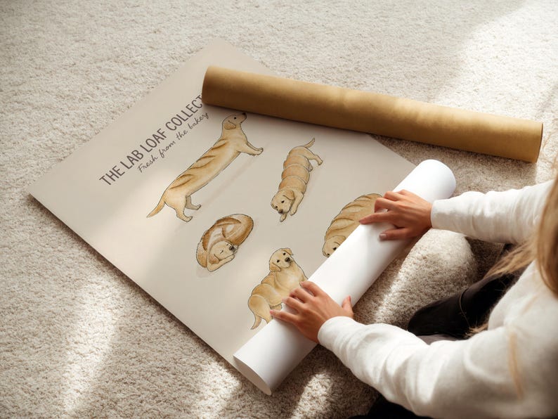 Puede incluir: Un p&oacute;ster beige titulado THE LAB LOAF COLLECTION Fresh from the bakery, que presenta ilustraciones de perros Labrador dorados con forma de varios panes, incluyendo un perro con forma de baguette, una hogaza redonda y otras posturas sentadas.