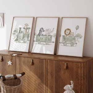 May include: Three framed wall art prints featuring watercolor illustrations of animals in green train cars. The first shows a giraffe in a locomotive, the second a zebra and elephant in a carriage, and the third a lion and cub holding a green balloon.