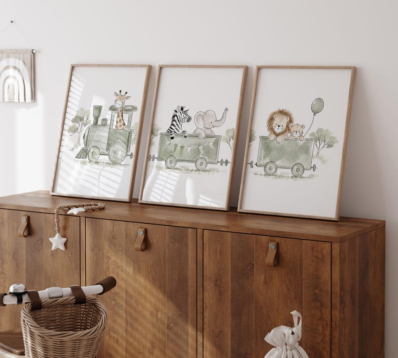 May include: Three framed wall art prints featuring watercolor illustrations of animals in green train cars. The first shows a giraffe in a locomotive, the second a zebra and elephant in a carriage, and the third a lion and cub holding a green balloon.