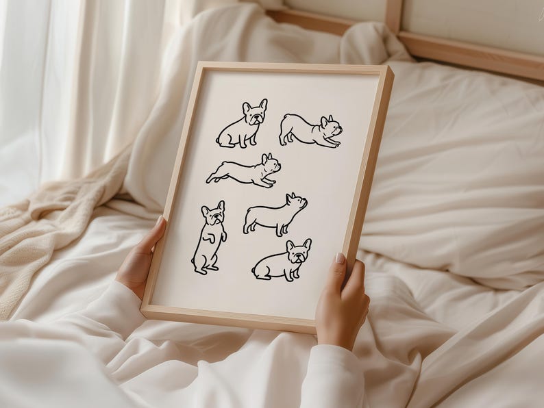 May include: A framed print featuring black line drawings of French Bulldogs in various poses. The dogs are depicted sitting, standing, and running on a cream-colored background. The frame is made of light-colored wood.