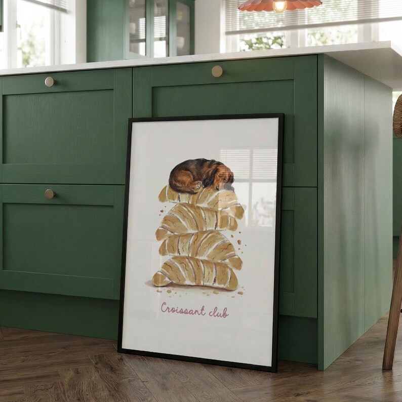 Puede incluir: Una l&aacute;mina art&iacute;stica vertical enmarcada con una ilustraci&oacute;n en acuarela de un perro peque&ntilde;o de color marr&oacute;n durmiendo sobre una pila de cuatro cruasanes dorados. El texto "Croissant club" aparece en cursiva rosa sobre el fondo blanco.