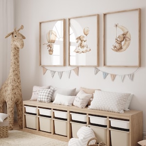 May include: A nursery scene featuring three framed watercolor prints with bunny illustrations. A woven giraffe stands beside a wooden storage unit with white bins. Pillows and a garland decorate the space, creating a cozy and inviting atmosphere.