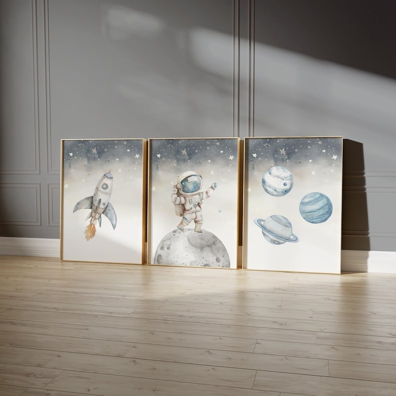 Pu&ograve; includere: Set di tre stampe artistiche incorniciate ad acquerello con illustrazioni a tema spaziale. Le stampe raffigurano un razzo, un astronauta sulla luna e pianeti su uno sfondo stellato. L'opera d'arte ha una palette di colori tenui e cornici dorate.