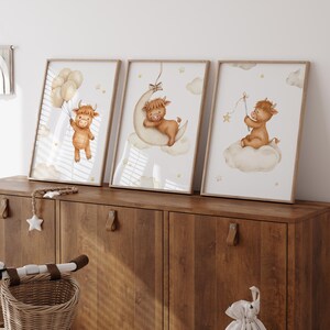 K&ouml;nnte beinhalten: Set aus drei gerahmten Aquarelldrucken mit einem Highland-Kuh-Thema. Ein Druck zeigt eine Kuh mit Luftballons, ein anderer auf einem Mond, und der dritte auf einer Wolke mit einem Stern. Die Drucke haben eine weiche, neutrale Farbpalette.