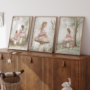 May include: Three framed watercolor prints featuring fairies in a whimsical forest setting. Each print showcases a fairy in a pink dress, perched on a mushroom. The artwork has a soft, pastel color palette with a dreamy, ethereal quality.