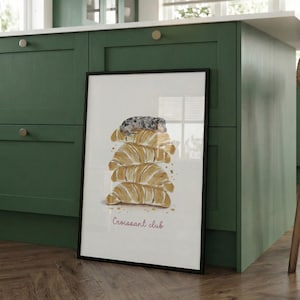 Puede incluir: Una l&aacute;mina art&iacute;stica vertical enmarcada con una ilustraci&oacute;n en acuarela de una pila de cuatro cruasanes dorados con un peque&ntilde;o perro gris moteado descansando encima. El texto "Croissant club" aparece en una fuente rosa sencilla debajo.
