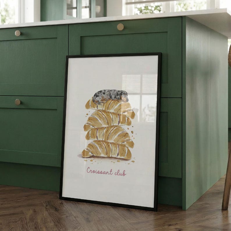 Puede incluir: Una l&aacute;mina art&iacute;stica vertical enmarcada con una ilustraci&oacute;n en acuarela de una pila de cuatro cruasanes dorados con un peque&ntilde;o perro gris moteado descansando encima. El texto "Croissant club" aparece en una fuente rosa sencilla debajo.