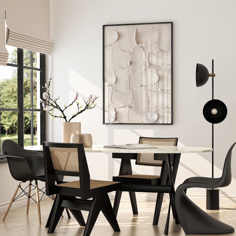 May include: A modern dining room with a white marble table and black chairs. The table is set with a magazine and a vase of pink flowers. A black floor lamp with a round shade stands in the corner.