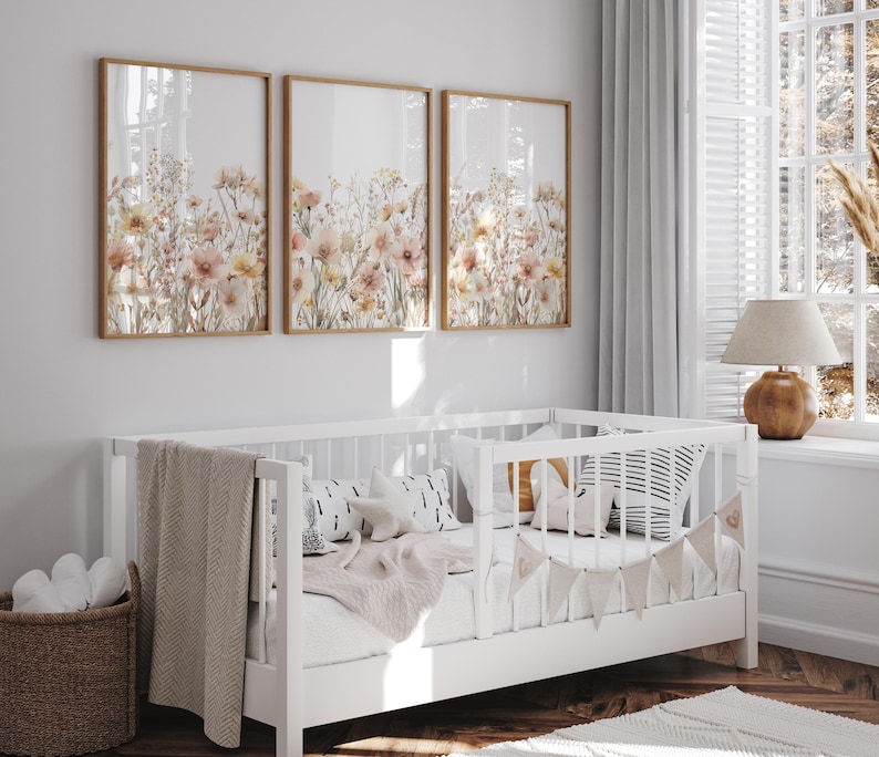 Puede incluir: Tres impresiones enmarcadas de arreglos florales de acuarela en tonos rosa, melocot&oacute;n y blanco. Las impresiones est&aacute;n colgadas en una pared blanca sobre una cuna blanca con una manta blanca y una almohada a rayas blancas y negras.