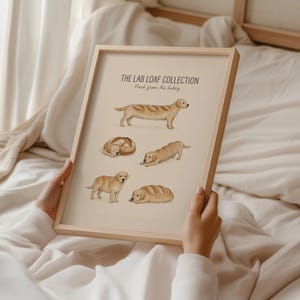 Puede incluir: Una l&aacute;mina enmarcada titulada THE LAB LOAF COLLECTION Fresh from the bakery, que presenta cinco ilustraciones de perros Labrador amarillos representados como varios tipos de panes, sobre un fondo beige claro en un marco de madera clara.