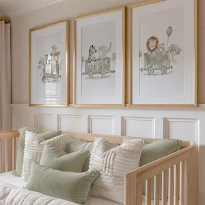 May include: Three framed wall art prints featuring watercolor illustrations of animals riding in train cars. The first shows a giraffe, the second a zebra and elephant, and the third a lion and cub with a balloon, all in gold frames.