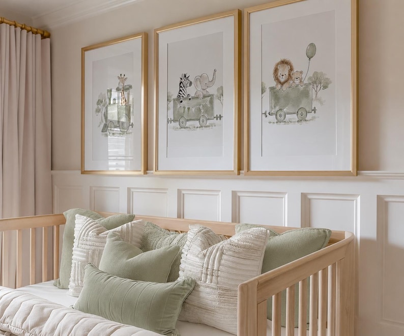 May include: Three framed wall art prints featuring watercolor illustrations of animals riding in train cars. The first shows a giraffe, the second a zebra and elephant, and the third a lion and cub with a balloon, all in gold frames.