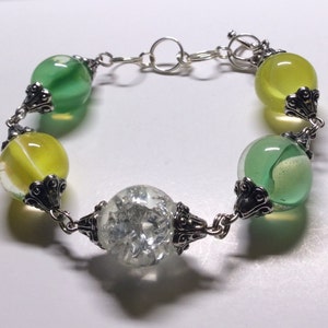 May include: A silver chain bracelet with five round glass beads. The beads are green, yellow, and clear. The beads have a silver metal accent on each side.