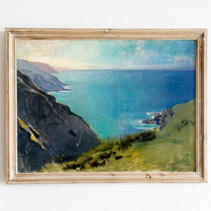 May include: Framed painting of a seascape with a rocky coastline and a blue ocean. The painting is in a light wood frame.