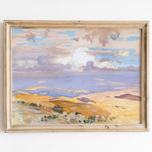 May include: A framed watercolor painting depicting a landscape with rolling hills and a cloudy sky. The hills are painted in shades of yellow, orange, and brown, while the sky is a mix of blue, purple, and white. The painting is framed in a simple wooden frame.