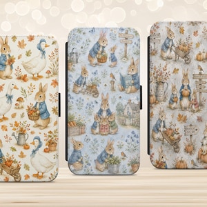 May include: Three rectangular phone cases featuring Peter Rabbit illustrations. The left case has a white background with rabbits, ducks, and autumn leaves. The centre case has a blue background with garden scenes. The right case features pumpkins and rabbits.