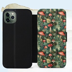 May include: A black leather phone case with a colorful mushroom and leaf pattern. The case is open, revealing the interior and the phone's camera. The design features red mushrooms with white spots, green leaves, and a dark green background.
