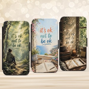 May include: Three phone cases with the text "it's ok not to be ok". The cases feature different scenic designs: a forest, a coastal view, and a cozy room with books and a window.