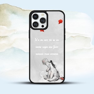 May include: A white phone case featuring a cartoon donkey and the quote "It's ok not to be ok. Some days are just harder than others." The case has a black border and a camera cutout.