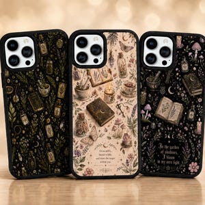 May include: Three phone cases with distinct designs. One case has a dark background with botanical illustrations and potion bottles. The second case features a cream background with a butterfly, books, and a candle. The third case has a dark background with text that reads "In the garden of shadows, I bloom in my own light."