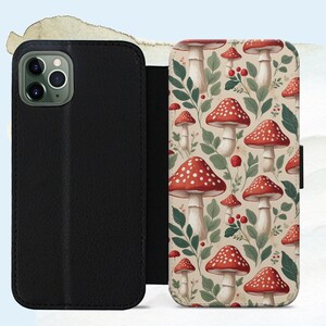 May include: Black leather phone case with a flap, open to reveal a whimsical pattern of red and white spotted mushrooms, green leaves, and berries on a beige background. The case is designed to protect the phone.
