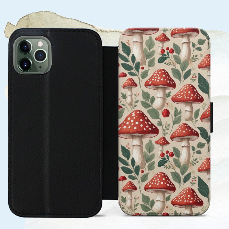 May include: Black leather phone case with a flap, open to reveal a whimsical pattern of red and white spotted mushrooms, green leaves, and berries on a beige background. The case is designed to protect the phone.