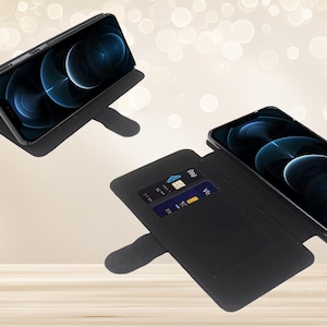 May include: Two black smartphone wallet cases shown in different positions. One case is propped up in a landscape viewing angle, while the other is open, displaying a smartphone screen and two interior card slots containing credit cards.