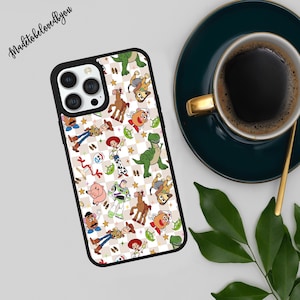 Puede incluir: Una funda de teléfono negra con un patrón colorido de personajes de dibujos animados sobre un fondo a cuadros. La funda tiene un borde negro y un recorte para la cámara. El texto "Madetobelovedbyyou" está en la esquina superior izquierda.