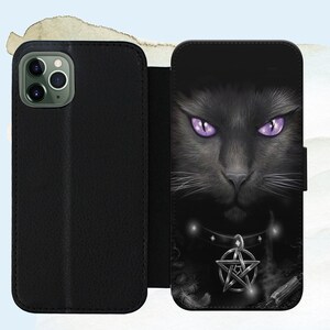 Puede incluir: Funda de tel&eacute;fono de cuero negro con un gato negro de ojos morados y un dije de pentagrama. La funda tiene una solapa que cubre la pantalla del tel&eacute;fono.
