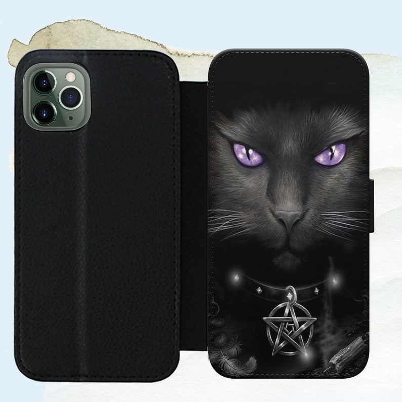 Puede incluir: Funda de tel&eacute;fono de cuero negro con un gato negro de ojos morados y un dije de pentagrama. La funda tiene una solapa que cubre la pantalla del tel&eacute;fono.