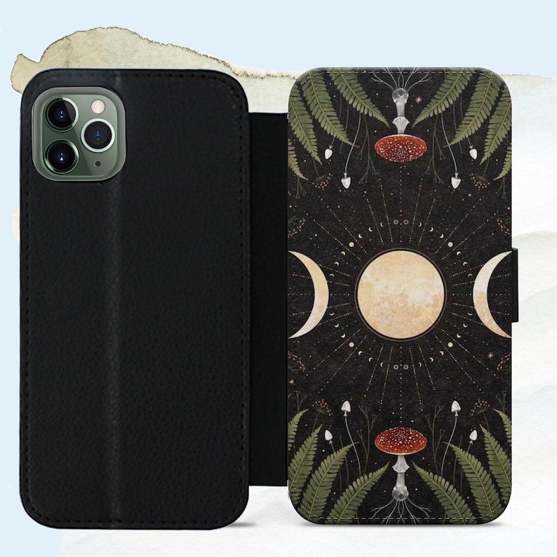 May include: Black leather phone case with a magnetic closure. The case features a detailed illustration of a celestial design with a full moon, crescent moons, mushrooms, and ferns on a dark background. The case is designed to protect the phone.