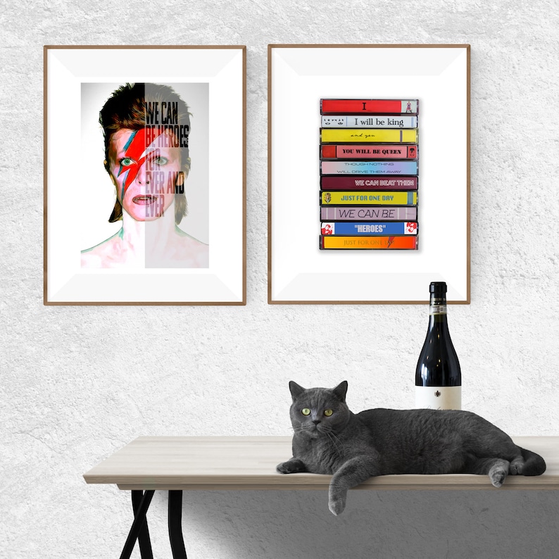 Może przedstawiać: Dwa oprawione wydruki Davida Bowie. Lewy wydruk przedstawia zbliżenie twarzy Bowie z napisami "We Can Be Heroes Ever and Ever" nałożonymi na jego twarz. Prawy wydruk przedstawia stos kaset magnetofonowych z tytułami album&oacute;w Bowie: "I Will Be King", "You Will Be Queen", "We Can Beat Them", "Just For One Day", "We Can Be", "Heroes", "Red Money" i "Low".