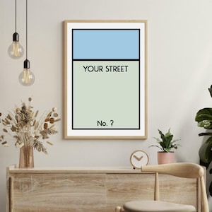 Può includere: Una stampa incorniciata con un design azzurro e verde, con il testo "YOUR STREET" e "No.?" in nero. L'opera d'arte è esposta su una parete colorata, con un mobile in legno e una sedia in primo piano.