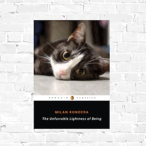 May include: A Penguin Classics paperback book cover featuring a black and white cat with yellow eyes. The title of the book is "The Unbearable Lightness of Being" by Milan Kundera.