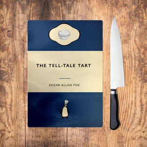 Puede incluir: Una tabla de cortar azul y dorada con el título "The Tell-Tale Tart" de Edgar Allan Poe. Una ilustración de pingüino se encuentra en la parte inferior de la tabla.