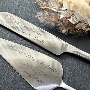 Può includere: Un set di due coltelli per torta d'argento con testo inciso. Il coltello superiore recita "Die geheime Zutat ist immer Liebe" con due cuori. Il coltello inferiore recita "Laura-Marie & Stefan 17.01.2024" con due cuori e un motivo floreale.