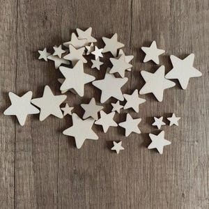 Könnte beinhalten: Eine Ansammlung von unbemalten Holzsternen in verschiedenen Größen, die auf einer Holzoberfläche angeordnet sind. Die Sterne sind unterschiedlich groß, von klein bis groß, mit sichtbarer Holzmaserung an den Kanten.