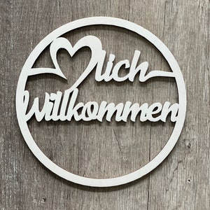 Könnte beinhalten: Weißer Holz-Kreis mit den Worten "Herzlich willkommen" und einem Herz-Ausschnitt.