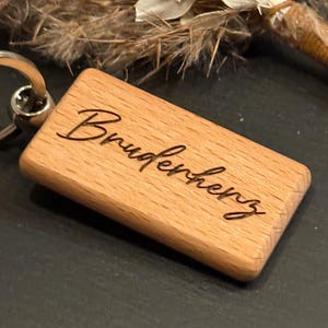May include: Wooden keychain with the word "Bruderherz" engraved on it. The keychain is attached to a silver ring.