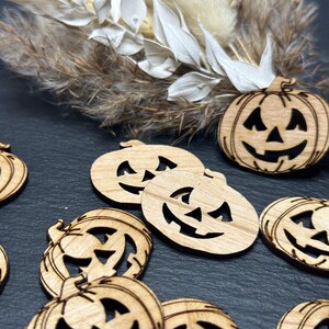 Könnte beinhalten: Eine Sammlung von Holz-Kürbis-Ornamenten mit geschnitzten Jack-o'-Lantern-Gesichtern. Die Kürbisse sind in verschiedenen Größen und auf einer dunklen Oberfläche angeordnet.