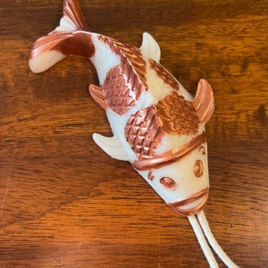May include: White and copper colored ceramic koi fish figurine with a white string attached to the bottom.