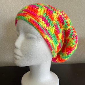 May include: A bright neon green, pink, yellow, and orange crocheted beanie hat. The hat is slouchy and has a loose fit.