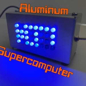 Puede incluir: Una pequeña caja plateada con una cuadrícula de luces azules y blancas. La caja está etiquetada "Aluminum Supercomputer" en texto naranja.