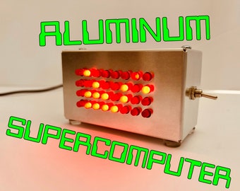 May include: A small, silver box with a grid of red and yellow lights. The box has a switch on the side and the words "ALUMINUM SUPERCOMPUTER" are written in green letters on the background.