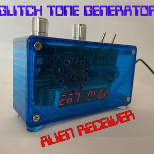 Może przedstawiać: Niebieskie plastikowe pudełko z czerwonym wyświetlaczem cyfrowym i dwoma srebrnymi pokrętłami. Pudełko ma napis "GLITCH TONE GENERATOR" i "ALIEN RECEIVER".