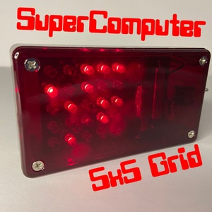 Puede incluir: Una caja rectangular roja con una cuadrícula de 25 LED rojos. La caja tiene una tapa de plástico transparente y está etiquetada como "SuperComputer 5x5 Grid".