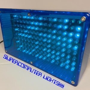 Op de afbeelding: Een blauwe, rechthoekige doos met een raster van blauwe lampjes erin. De doos is gemaakt van doorzichtig plastic en heeft een zwart snoer eraan bevestigd. De tekst "SUPERCOMPUTER LIGHTS!!!" staat op de onderkant van de doos.