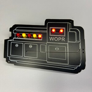 May include: A black WOPR computer system replica with a series of red and yellow lights on the top. The lights are lit up and the text "WOPR" is visible on the front of the system.